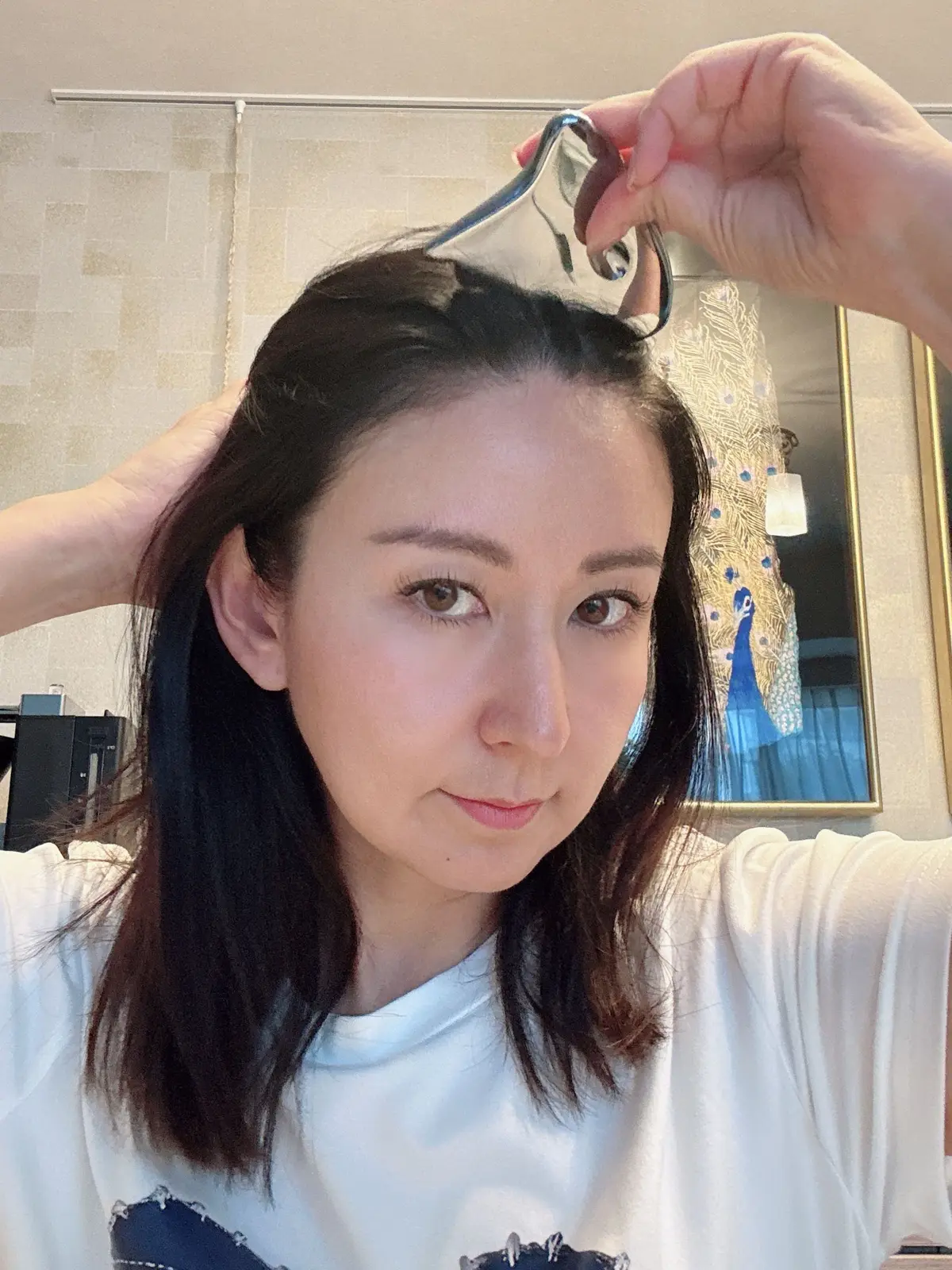 女性が鏡を見ながらヘアピンで髪を整えている。背景には羽毛の絵が飾られている。
