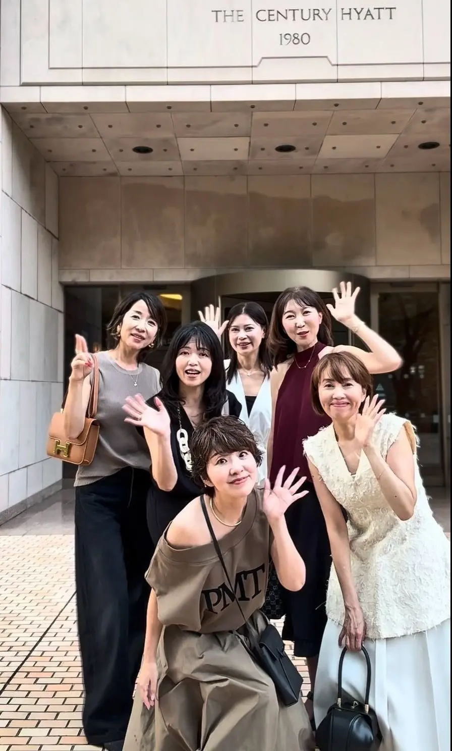 The Century Hyatt 1980と書かれたホテルの入り口前で、7人の女性が笑顔でポーズをとっている。手で「V」サインをしている人が複数いる。