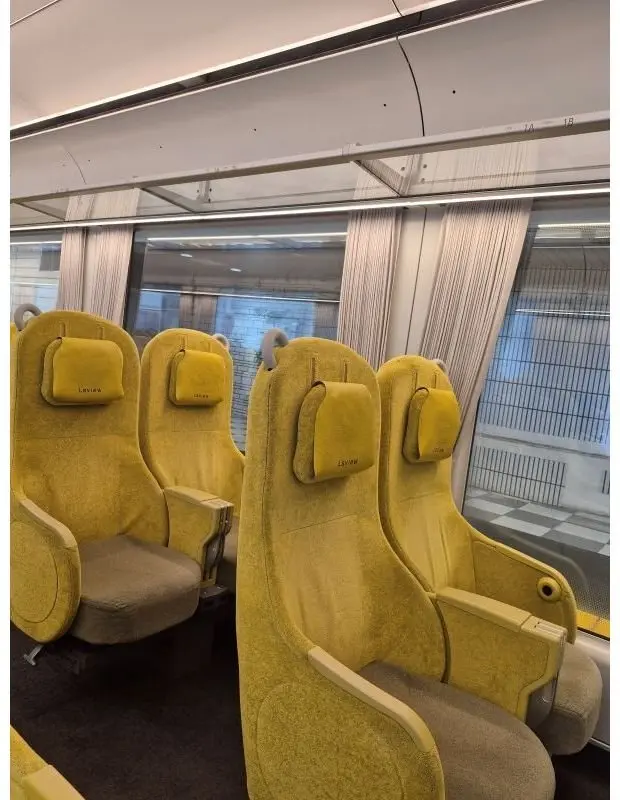 黄色い座席が並ぶ鉄道車両の内部。座席には「Laview」の文字が刺繍されている。窓から景色が見え、カーテンが設置されている。