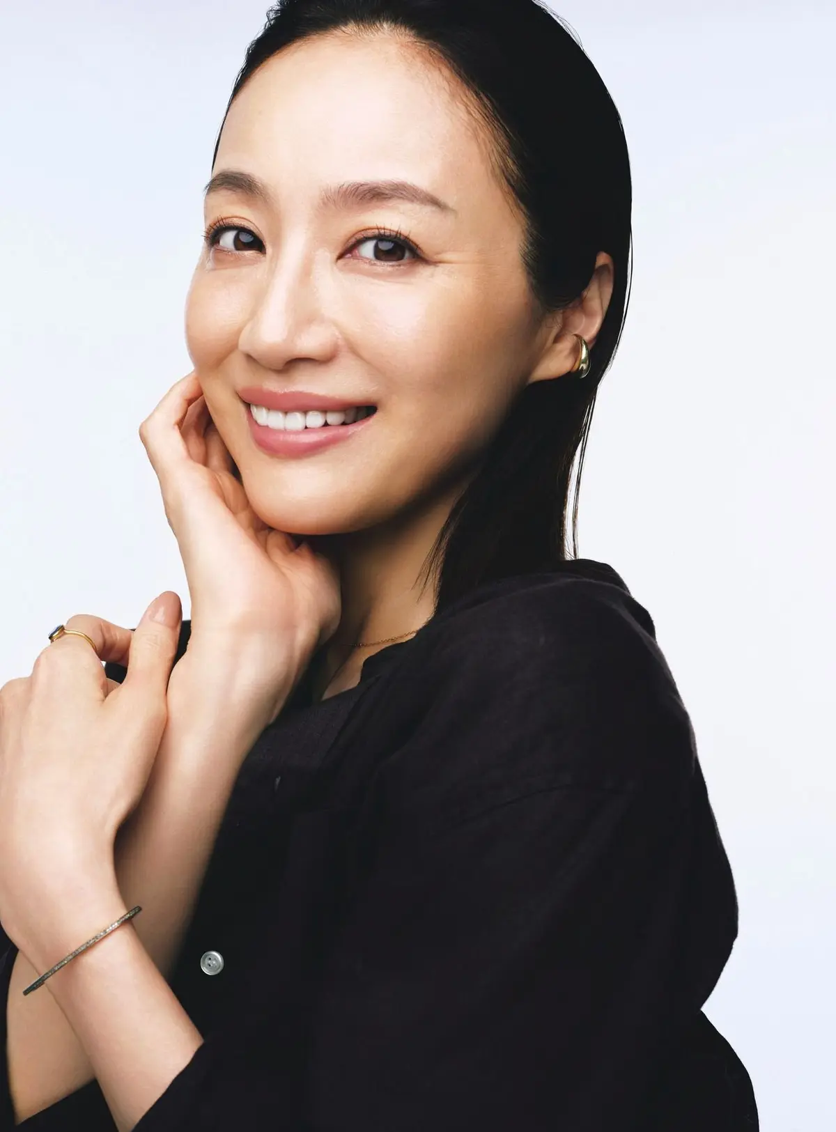 黒いトップスを着たアジア系の女性が、微笑みながらこちらを見ているポートレート。髪は後ろでまとめられ、耳には控えめなピアスをしている。手で頬を支え、上品な印象。