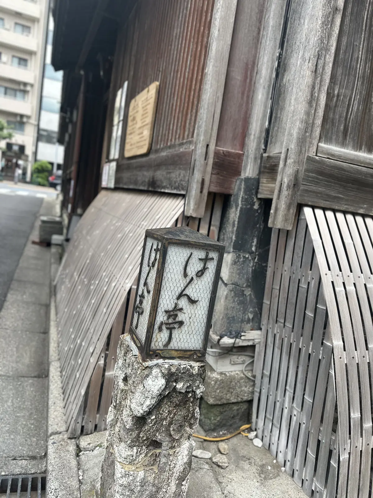 石の柱の上に設置された、竹製の格子で囲まれた灯篭。灯篭には「五反田」の文字が記されている。背景には木造の建物と現代の高層ビルが並ぶ。