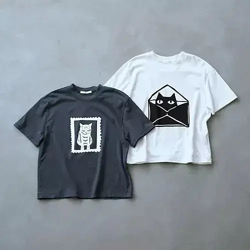 左は濃いグレーのTシャツ、右は白のTシャツ。それぞれ胸元に黒のイラストがプリントされている。左は猫の郵便切手風、右は猫のシルエットが入った封筒のデザイン。