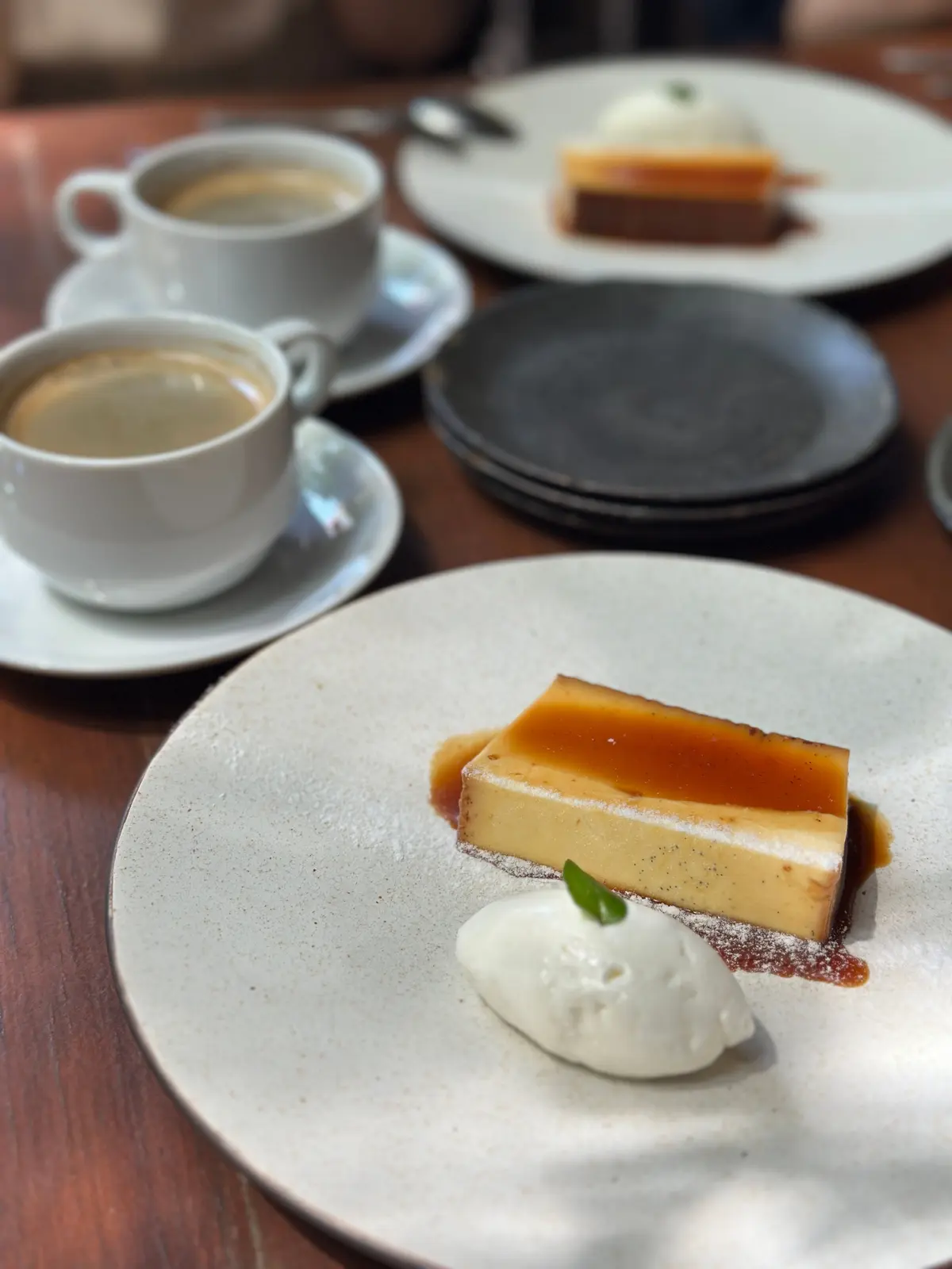 白いプレートにプリンと生クリーム、木製テーブルにコーヒーカップが並ぶ