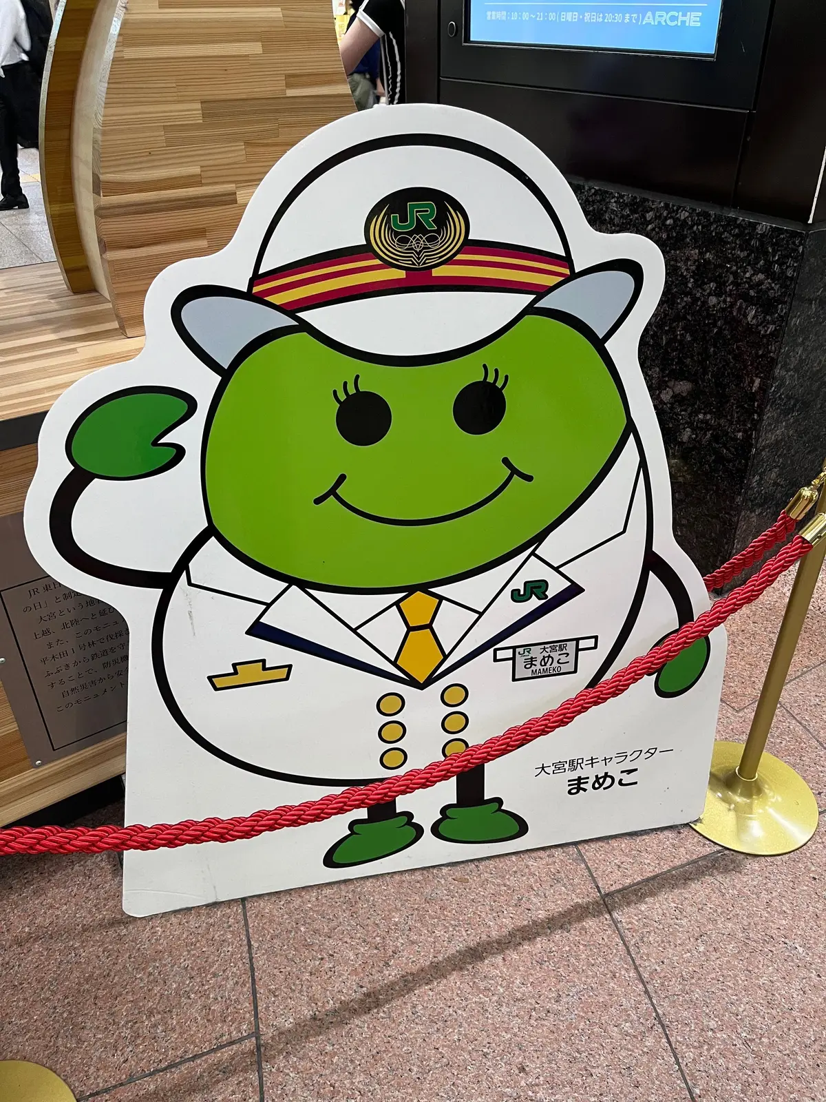 緑色のキャラクターが制服を着て、JRのロゴと「まめこ」という文字と共に、駅構内のコーナーで案内用の立体ディスプレイとして設置されている