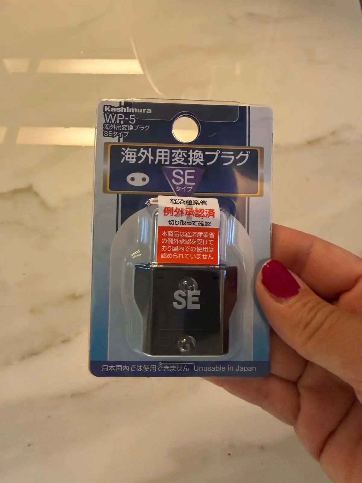 海外用変電プラグの青いパッケージで、SEと書かれた黒いプラグが中に入っている