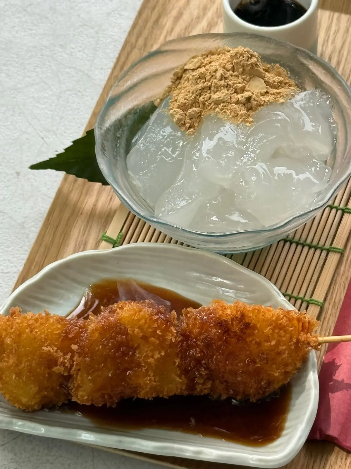 木製のトレーに、透明な器に入った白玉とكنجا、小皿に入った揚げ物と醤油が置かれている。白玉にはكنجاが乗せられ、緑色の葉が添えられている。