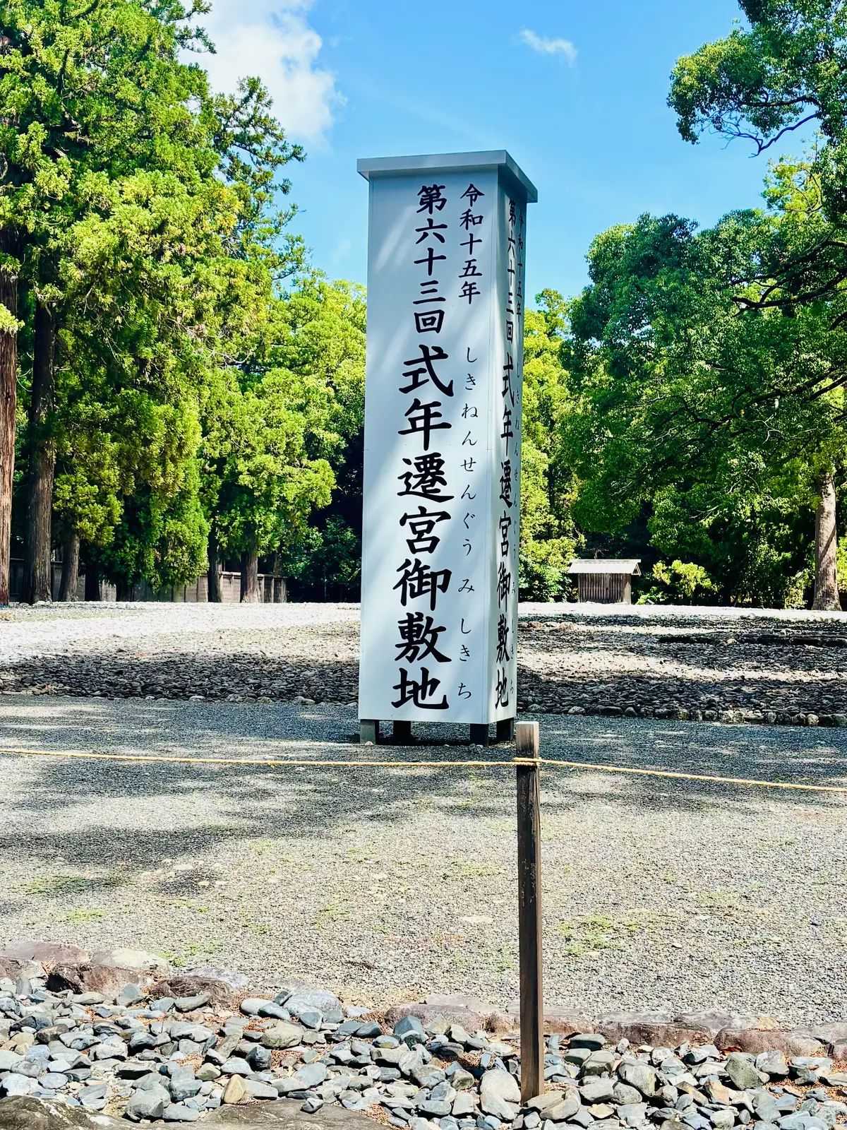 石畳の道脇に立つ、濃い青色の柱状の看板。黒い文字で「第六十三回 天遥宮御敷地」と書かれている。背景には緑豊かな木々が見える。