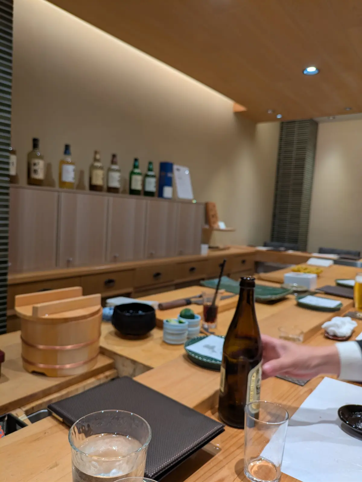 寿司盛り合わせにわさびをふりかける手、木製の台に置かれた料理と調味料