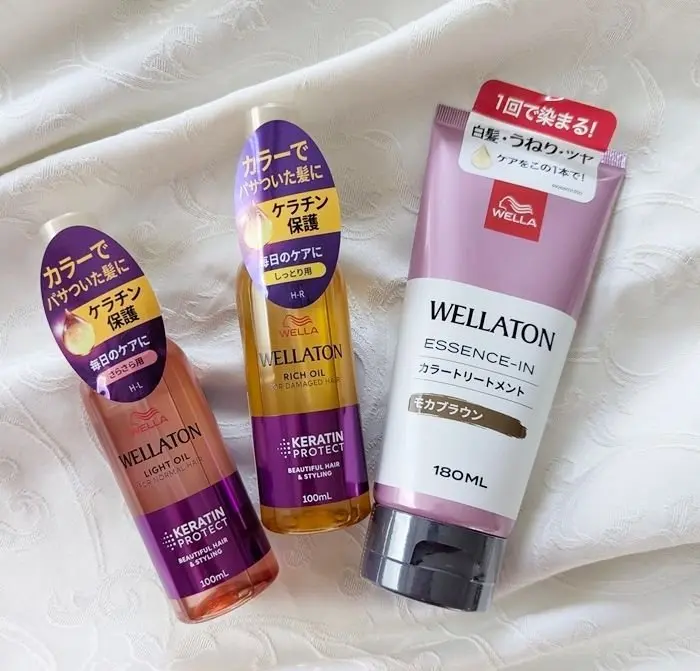白いシーツの上に置かれた、ウェラ（Wella）のヘアケア製品3点。左から、ライトオイル、リッチオイル、エッセンスインの順に並んでいる。それぞれ異なる色合いのボトルで、日本語のラベルが貼られている。