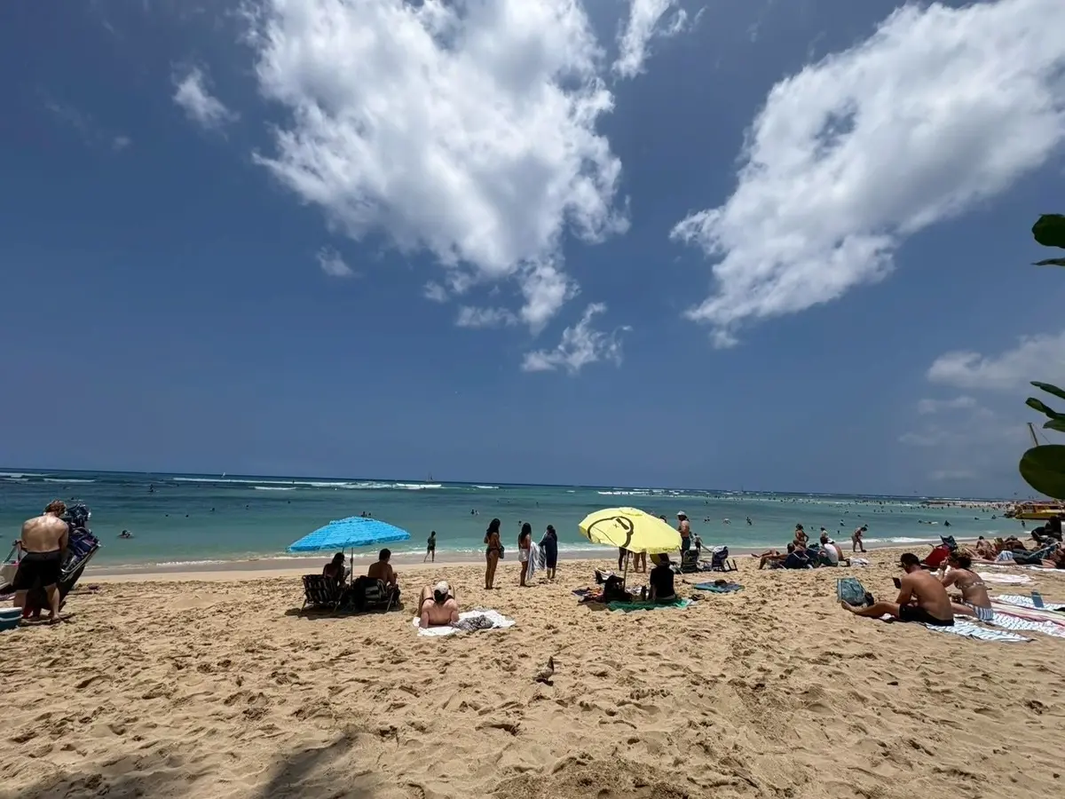 ビーチで多くの人がリラックスし、青い海と白い雲が広がる背景に、青と黄色の傘が置かれている