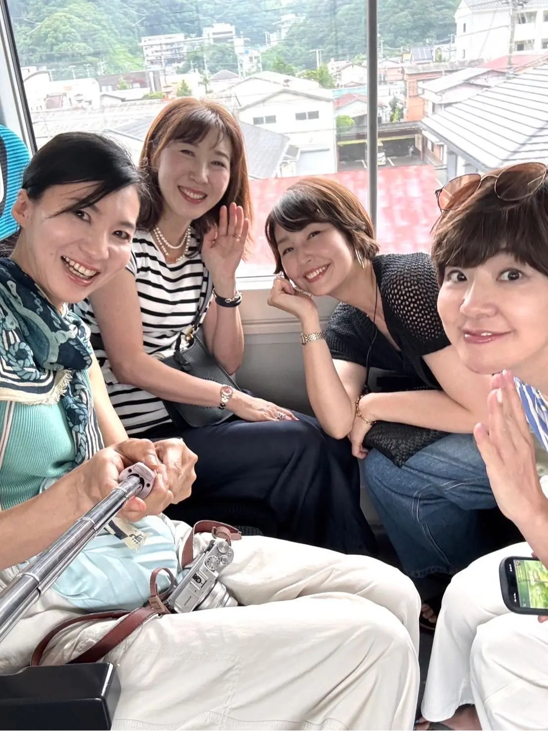 ケーブルカー内にて、4人の女性が窓の外の住宅地を見ながら笑い、楽しそうに会話している。