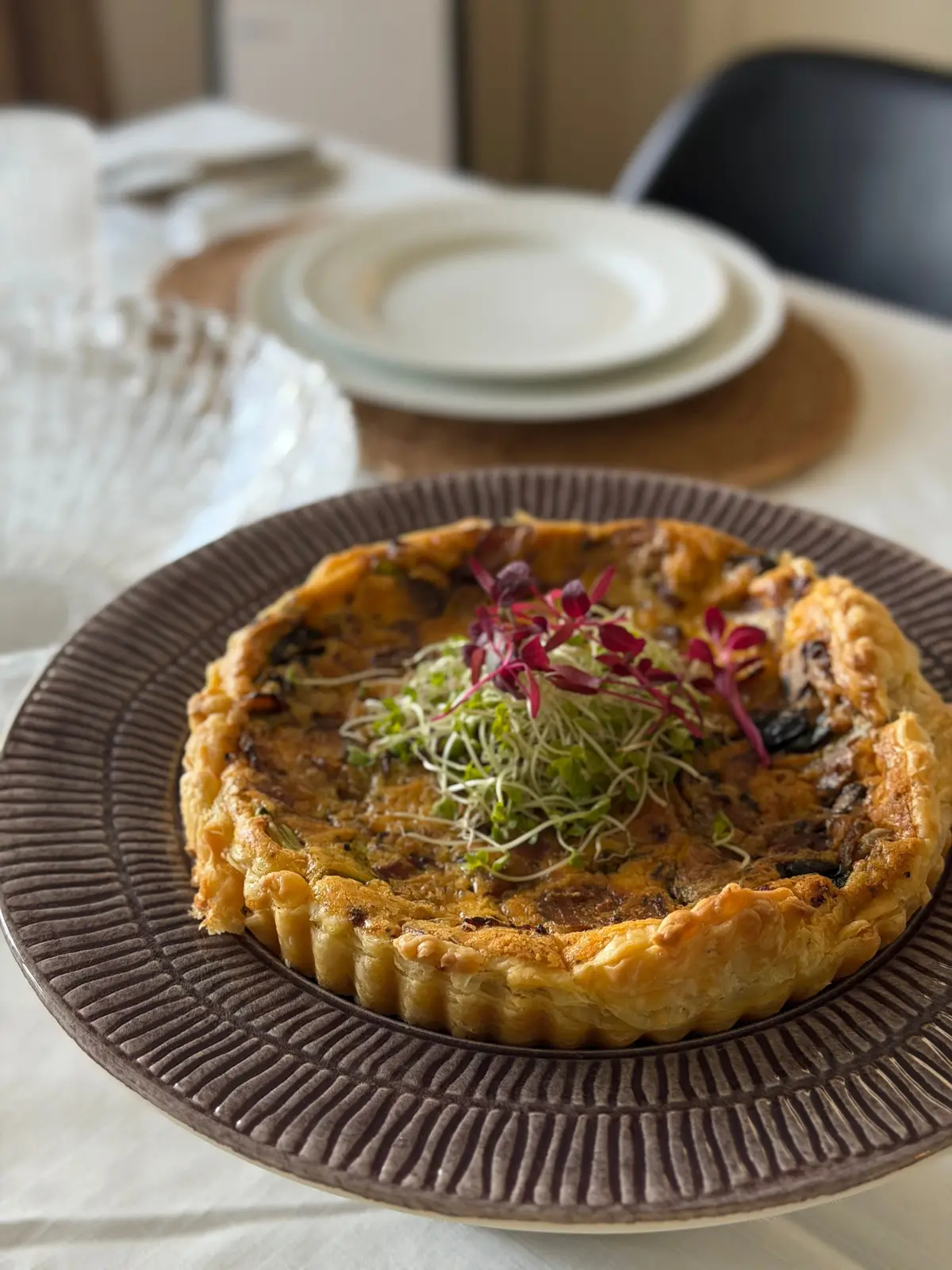 茶色いパイ皿にのったキッシュで、赤と緑の新芽がトッピングされています。