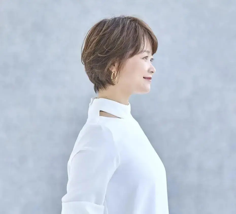 ショートヘアの女性が白い服を着て、左を向いて微笑んでいる。耳飾りが付いている。