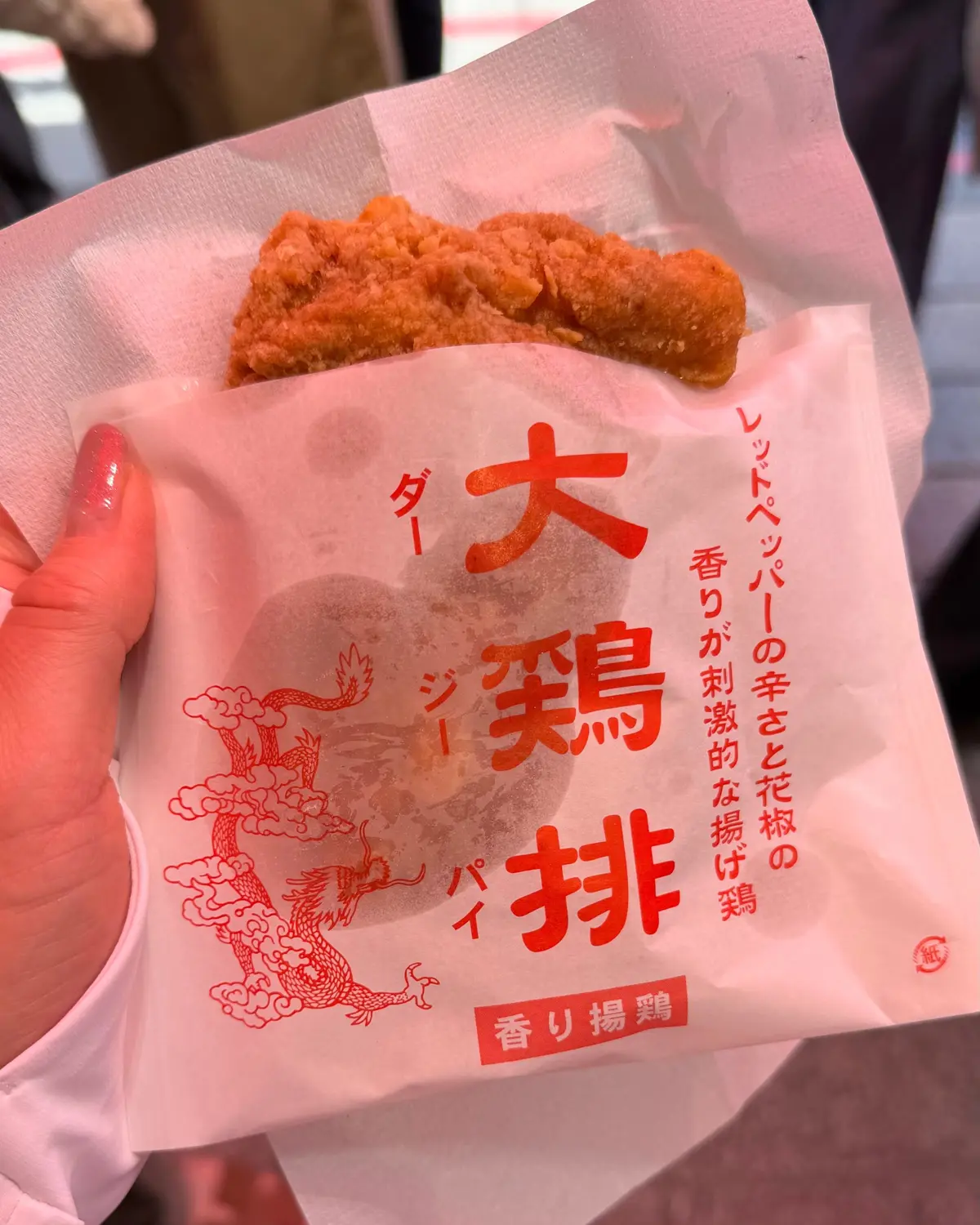 手で持つ紙パックに、きつね色で揚げられたエビの天ぷら。赤い文字で「大天ぷら」と表示され、龍の模様が背景にある。