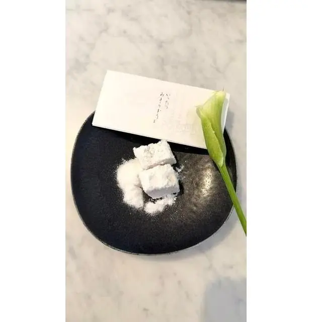 黒いプレートに白い花と白いカードが置かれた料理写真。プレートには粉状の物質と四角い白い塊が散らばっている。