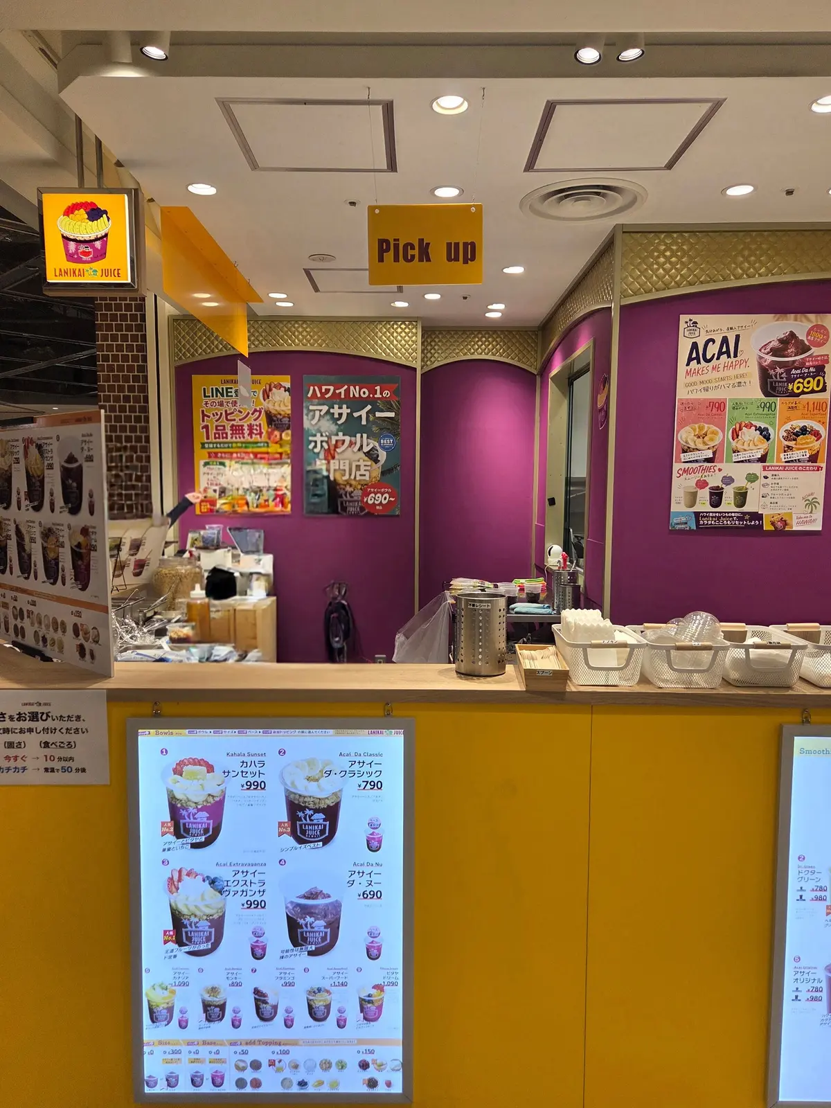 LANIHA JUICEの店舗内。カウンターがあり、デジタルメニューが設置されている。壁にはアサイーボウルの広告やメニューが掲示され、ショーケースにはドリンクや焼き菓子が並んでいる。