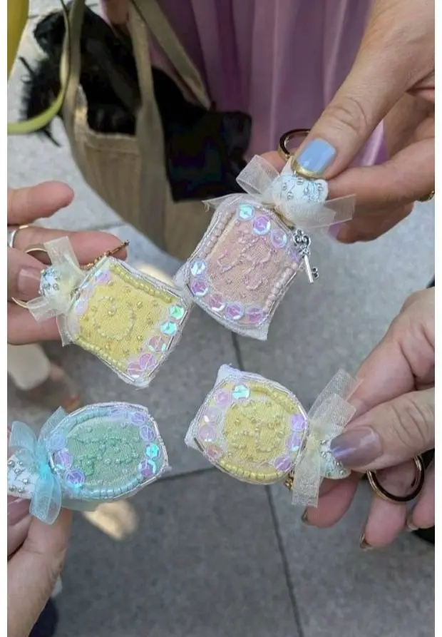 手で持つ小さなキーホルダー4個。各キーホルダーはリボン付きで、黄色、ピンク、青の生地と宝石のような装飾が施されている。