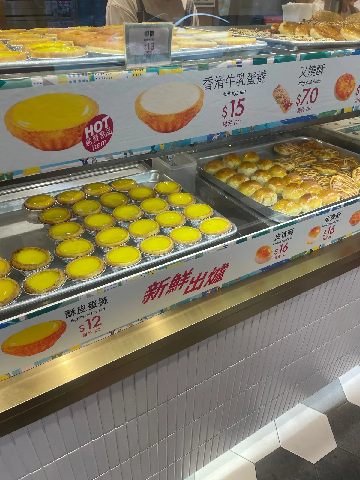黄色の卵タルトと蒸しパンが並ぶパティスリーショーケース、価格表示付き