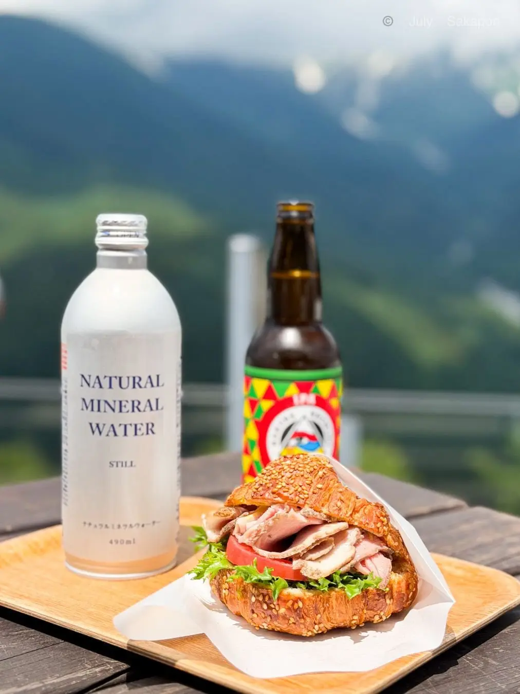 ナチュラルミネラルウォーターとビールボトル、トマトとレタスを挟んだセブンミールサンドイッチが木製プレートに並ぶ