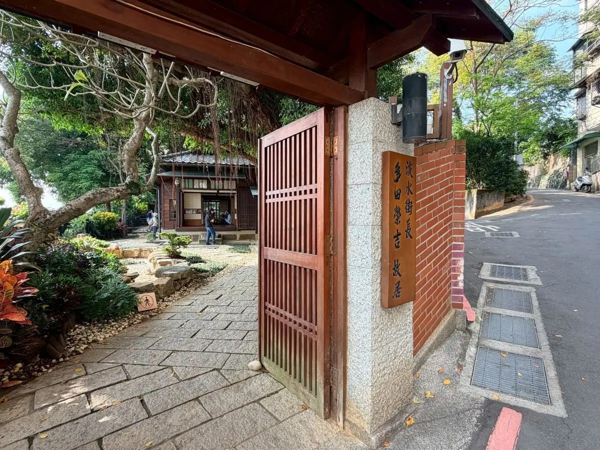 淡水街長多田栄吉故居。木製の門が石の柱に付いた道を挟んで立ち、伝統的な建物が背景に見える静かな路地