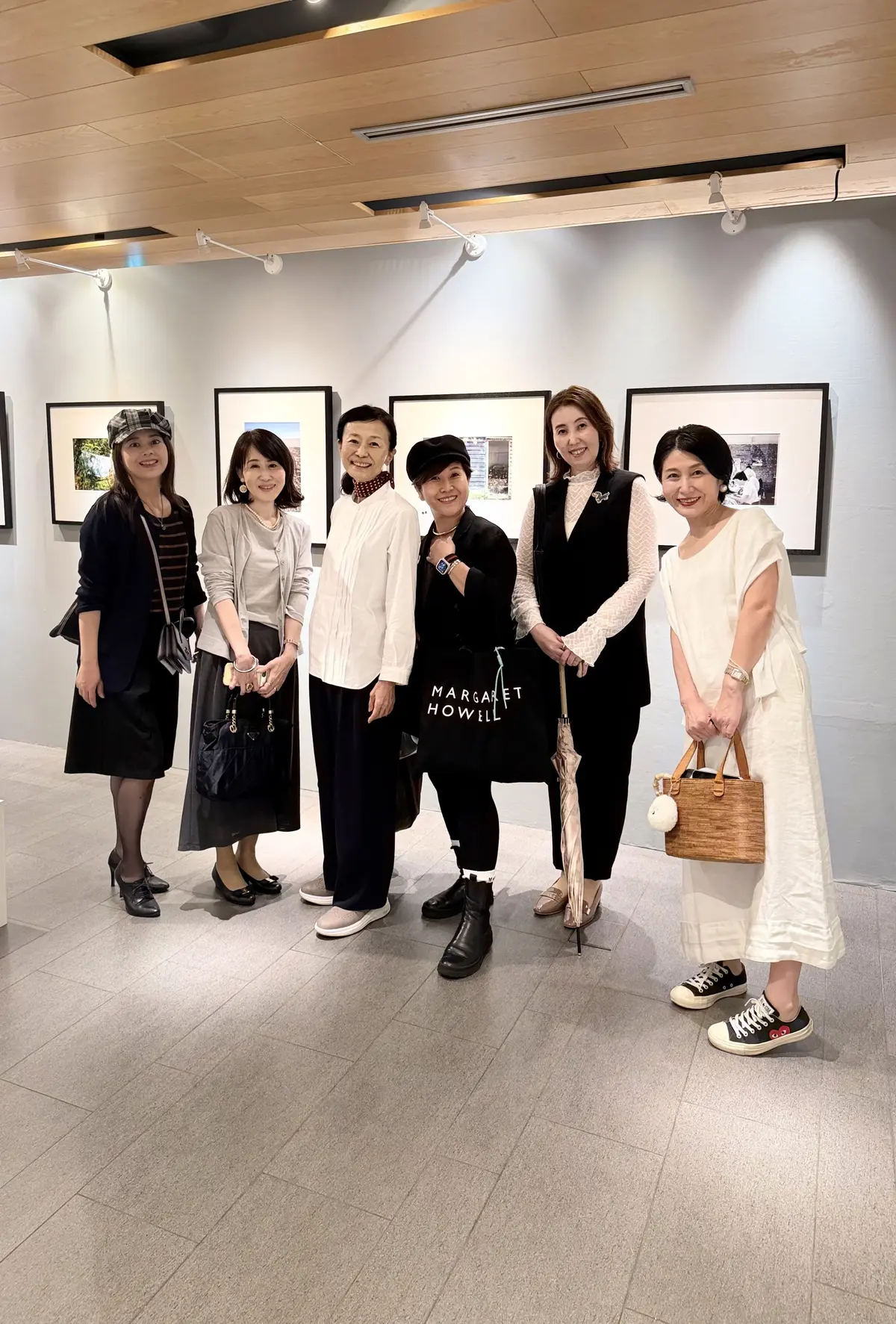 6人の女性が、壁に飾られた白黒写真の展示会場で並んで立っている。