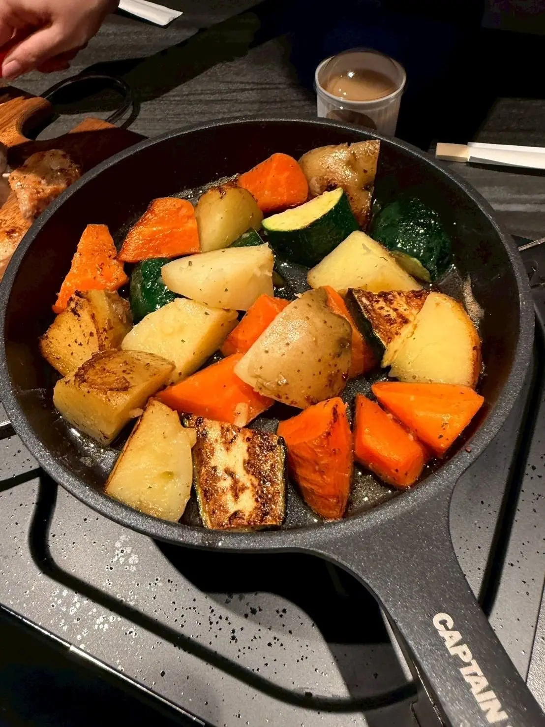 黒い鉄製のフライパンに入った、ロースト野菜。人参、ズッキーニ、じゃがいもが角切りになり、黒胡椒がふりかけられている。フライパンの取っ手に「CAPTAIN」の文字が見える。