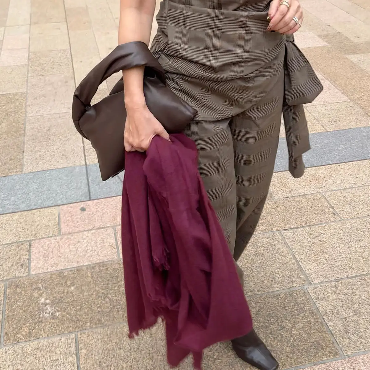 グレンチェックのセットアップに、深紅のストールを巻いた女性。茶色のレザーバッグを肩にかけ、黒いパンプスを履いている。