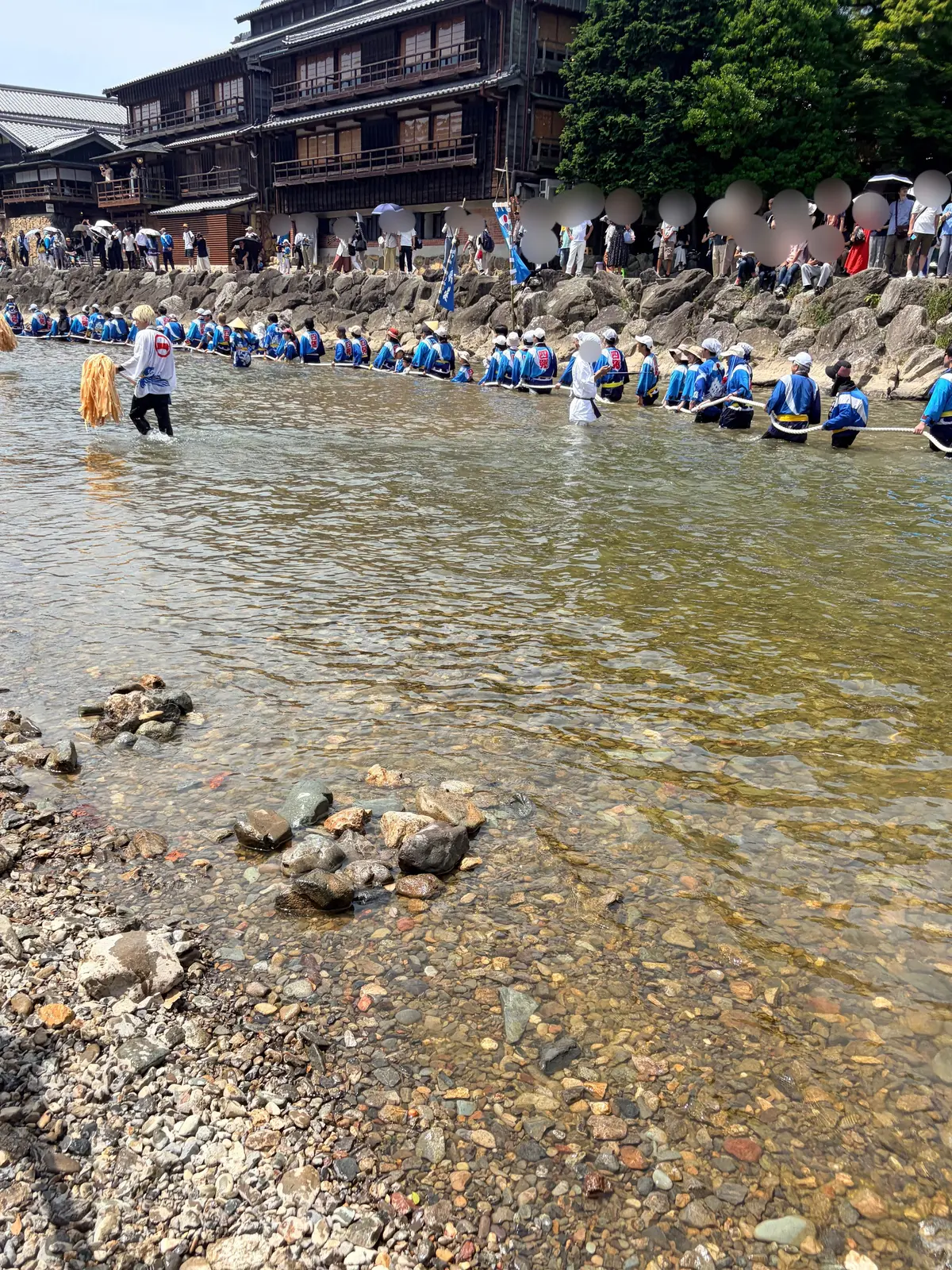 水中に足をつけて立つ人々が、麦わらの笠をかぶり、青い装束を身につけている。背景には建物と観客が並ぶ。