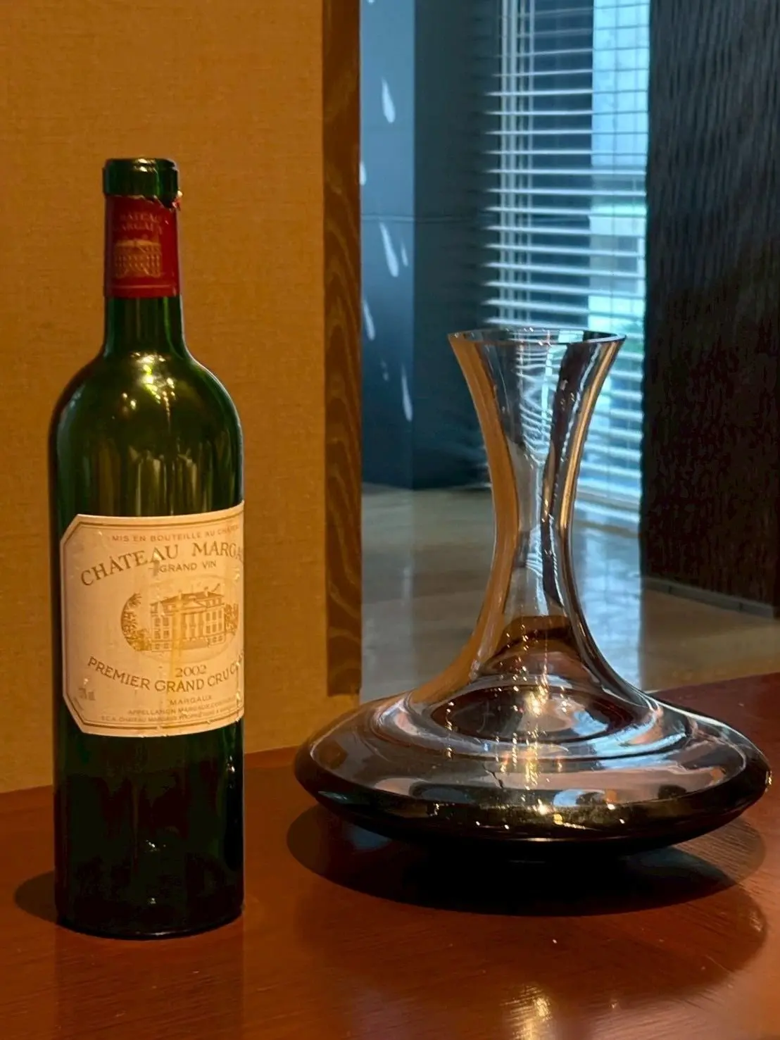 ワインボトルとデカンタ。ボトルには「CHATEAU MARGAUX」と「PREMIER GRAND CRU」の文字が見える。木製のテーブルに置かれ、背景には窓と壁がある。