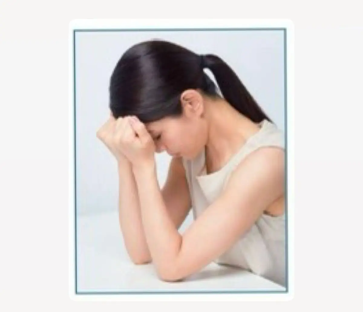 うつむき加減に、白いタンクトップを着た若い女性。両手で額を覆い、悲しげな表情をしている。背景は白っぽい壁。