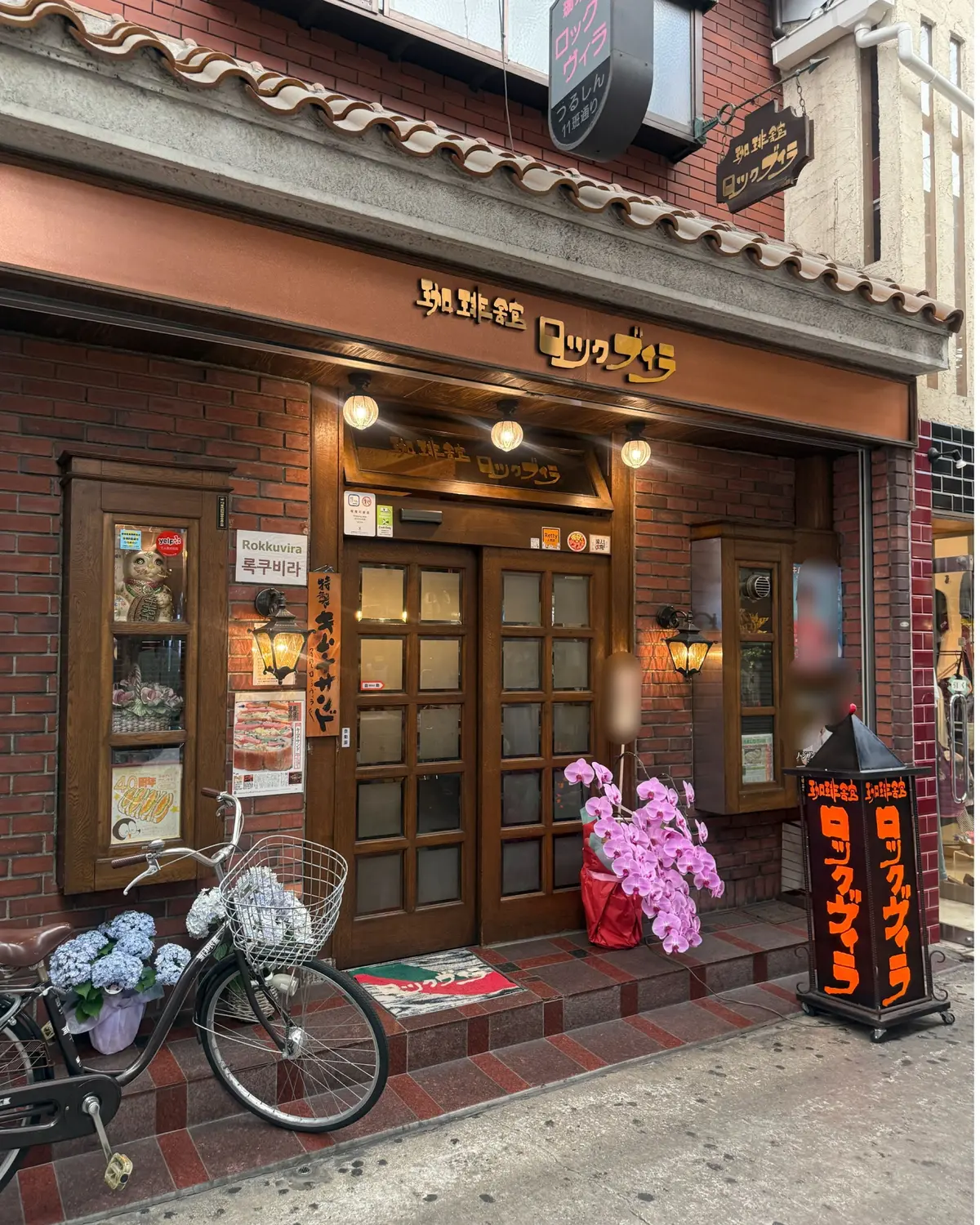 レトロな外観の喫茶店「ロクビラ」の入口、花と自転車が置かれた店前