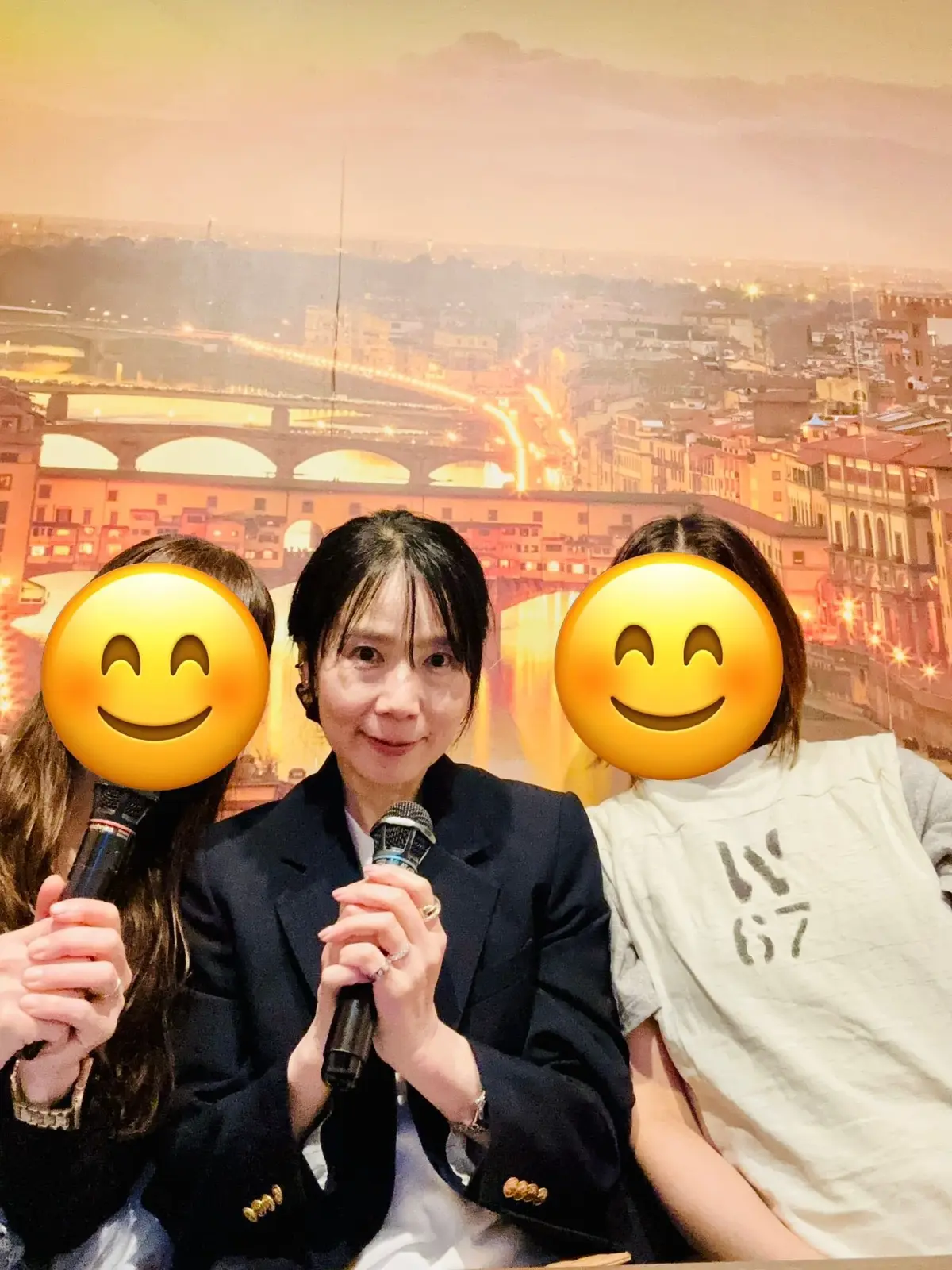 中央に女性がマイクを持ち、左と右に黄色い笑顔の絵文字が置かれた夜の街並みの背景