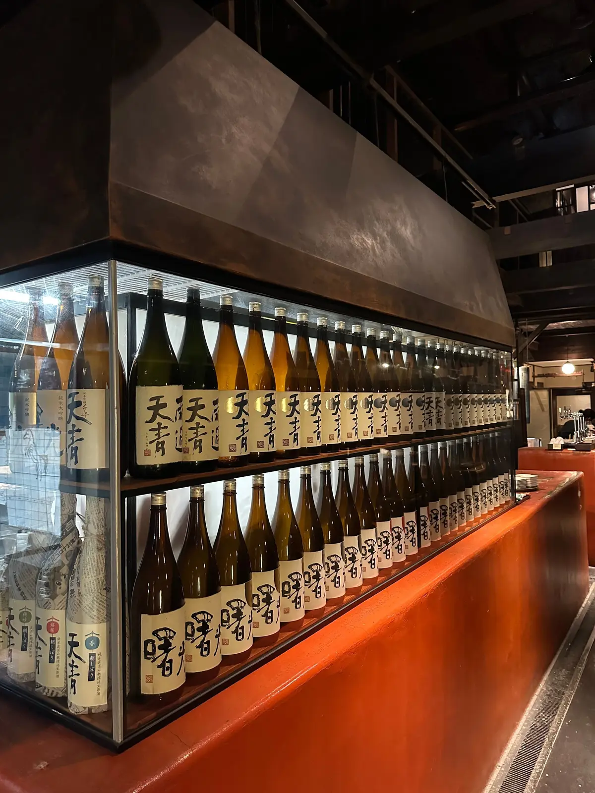 複数の日本酒のボトルがガラス棚に整列、ラベルに日本語の文字が記載されている