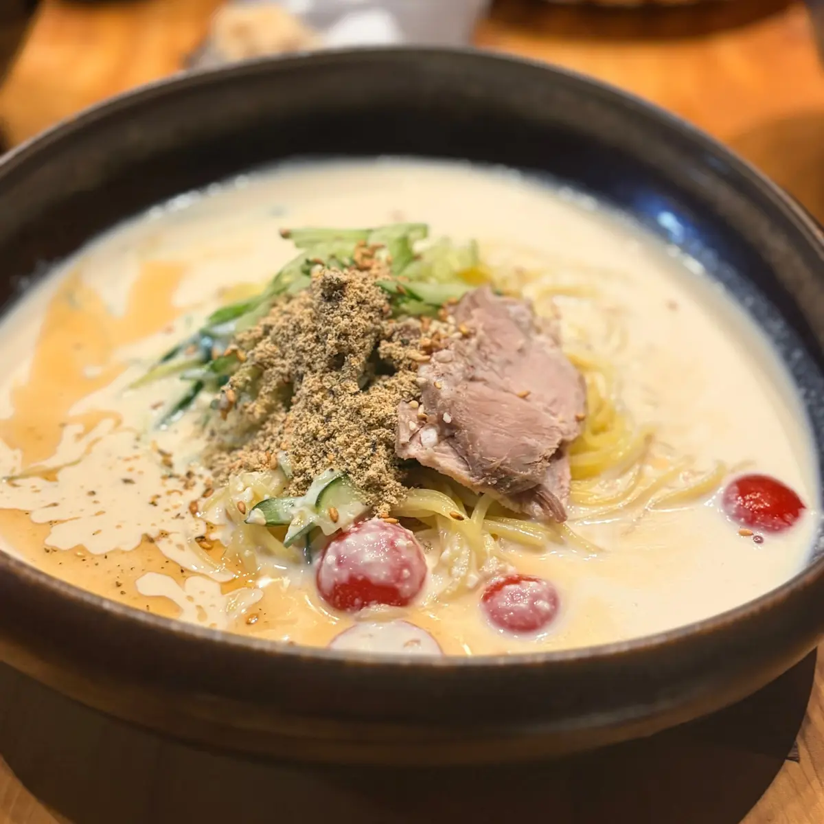 黒い丼に入ったラーメン。白濁したスープ、黄色の麺、薄切り肉、ネギ、赤い実が乗っている。表面には茶色い粉が振りかけられている。