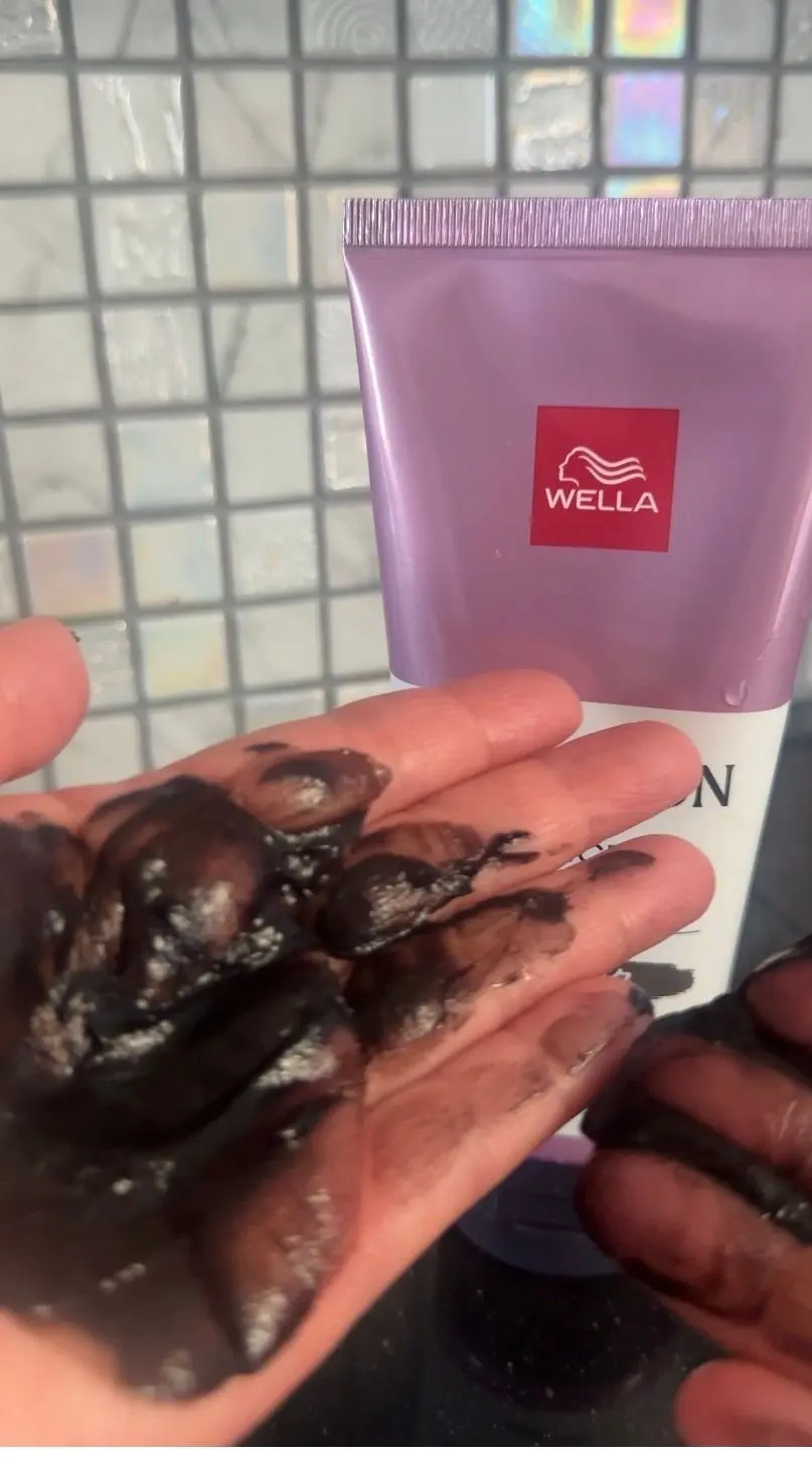 手に塗られたウェラ社のヘアカラー剤。濃い茶色のクリーム状で、手の一部が染まっている。背景にはタイル状の壁。