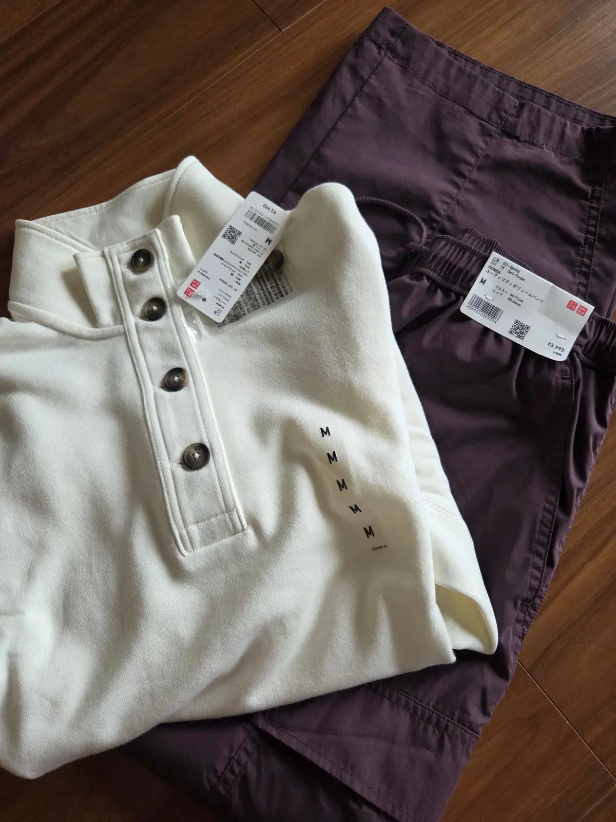 木製の床に置かれた、ユニクロの白と紫のショートパンツ2着。白はボタン付きのハイウエストで、紫は裾が絞られたデザイン。それぞれのタグには「M」と記載されている。