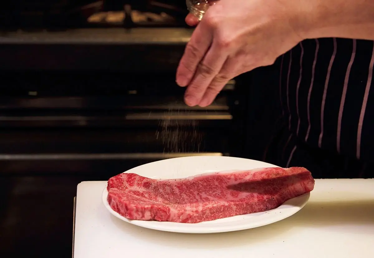 肉の両面に塩、次にこしょうをふる。
やや高い位置からふると、まんべんなく
ふりやすい（肉の厚さが1㎝程度の場合は、
常温に戻しておかなくてよい）。