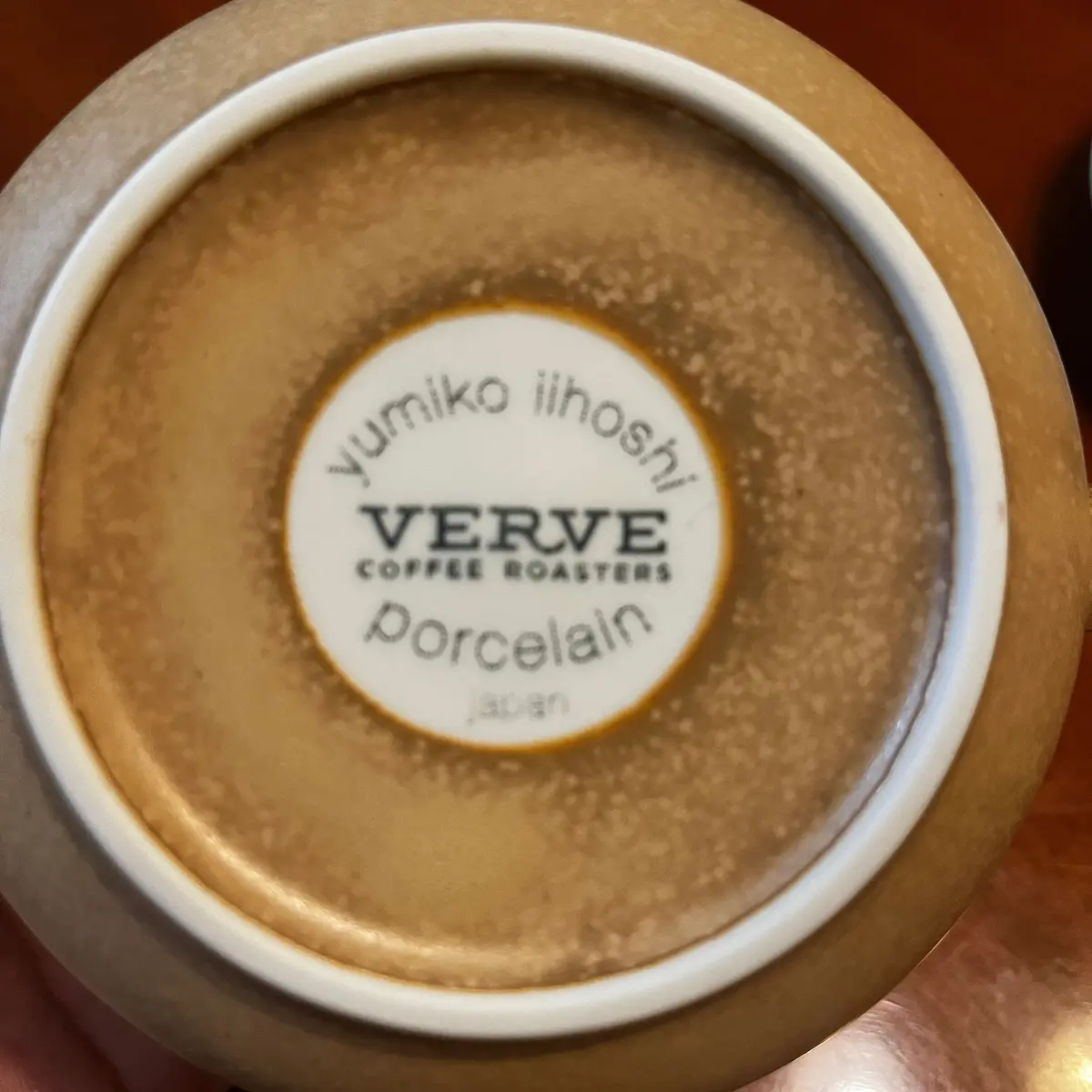 底面が黄色と白の模様の陶器製のカップ。中央に「yumiko iihoshi VERVE COFFEE ROASTERS Porcelain Japan」と記載された白いラベルが貼られている。