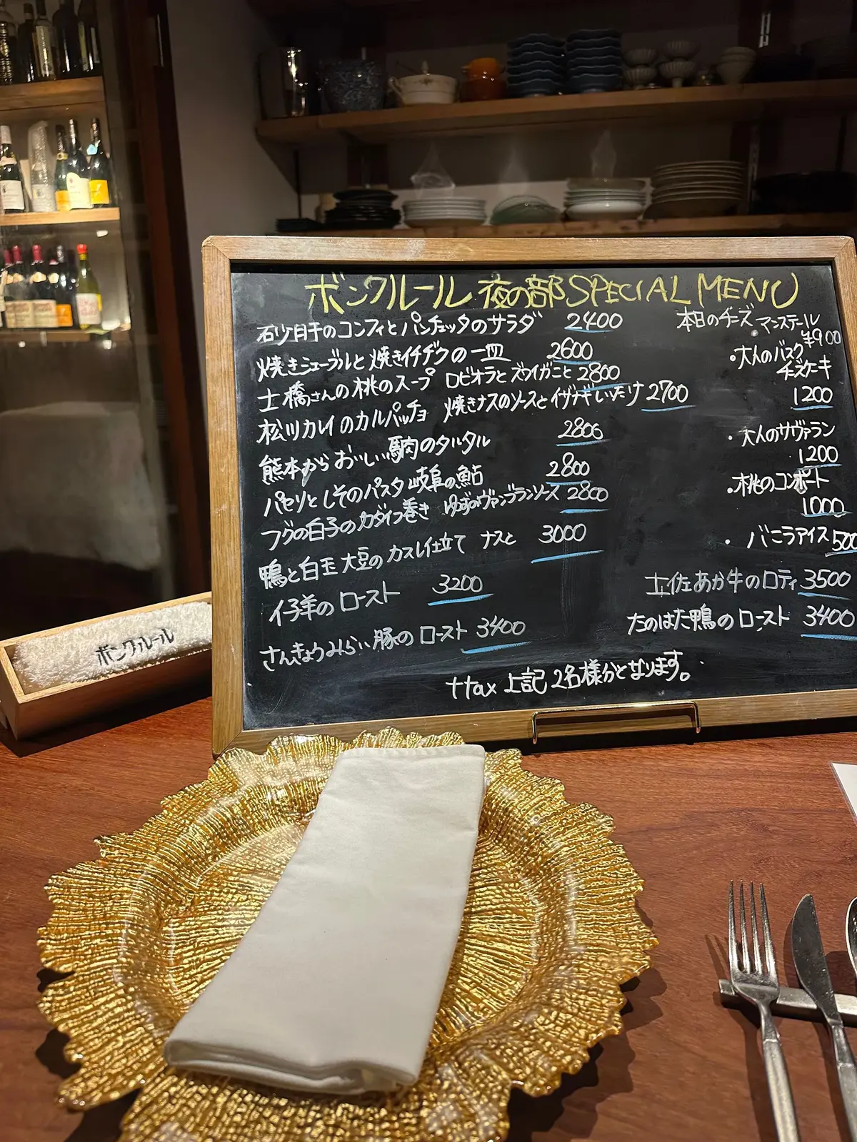 木製のテーブルに置かれた黒板に書かれた、ボンクール（Bon Courage）の季節限定スペシャルメニュー。手書き風の文字で料理名と価格が列挙されており、右下には「今日のオススメ」と書かれたメニューも記載されている。