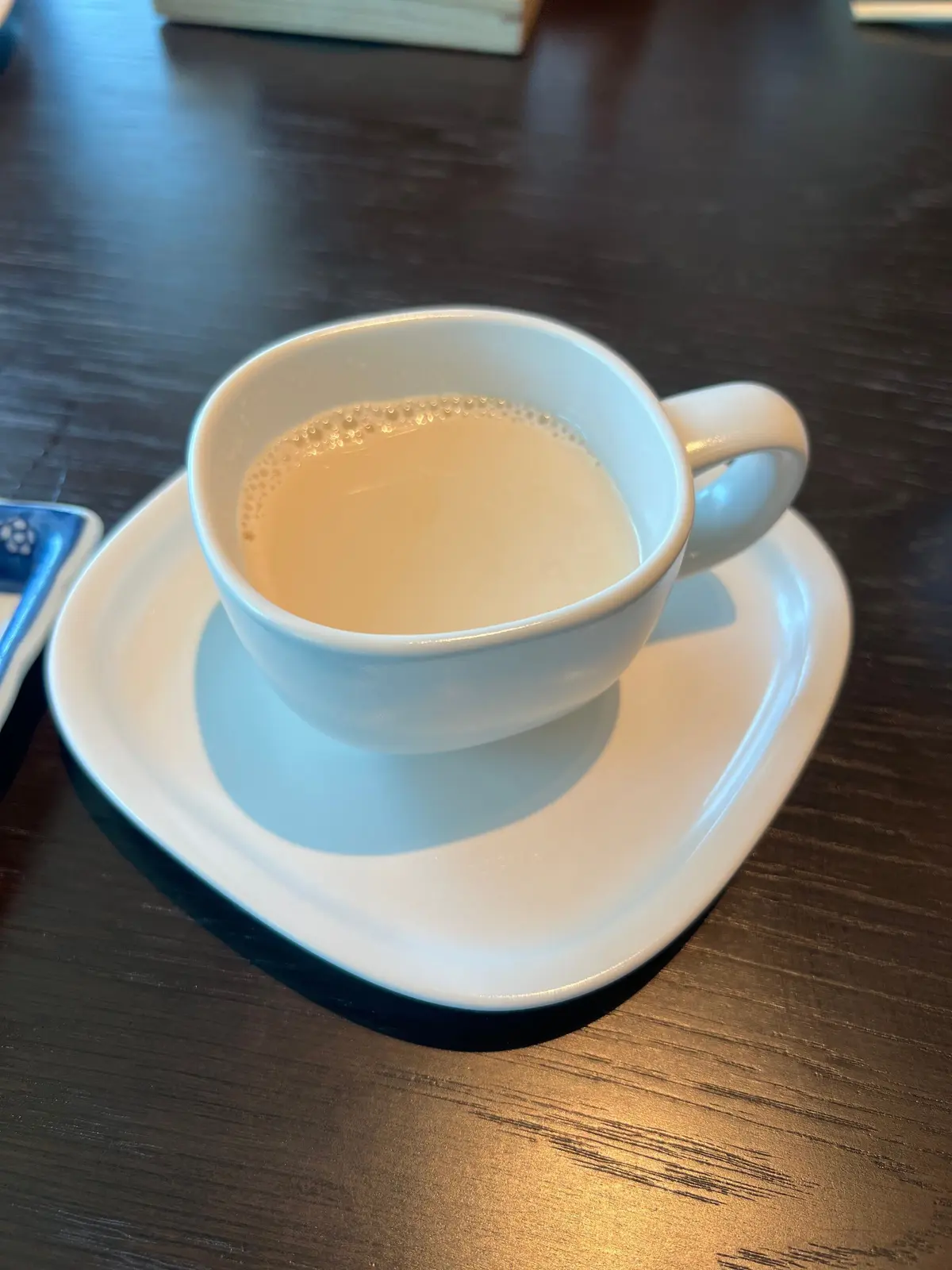 白いマグカップに茶色い飲み物が乗せられ、木製テーブルに置かれている