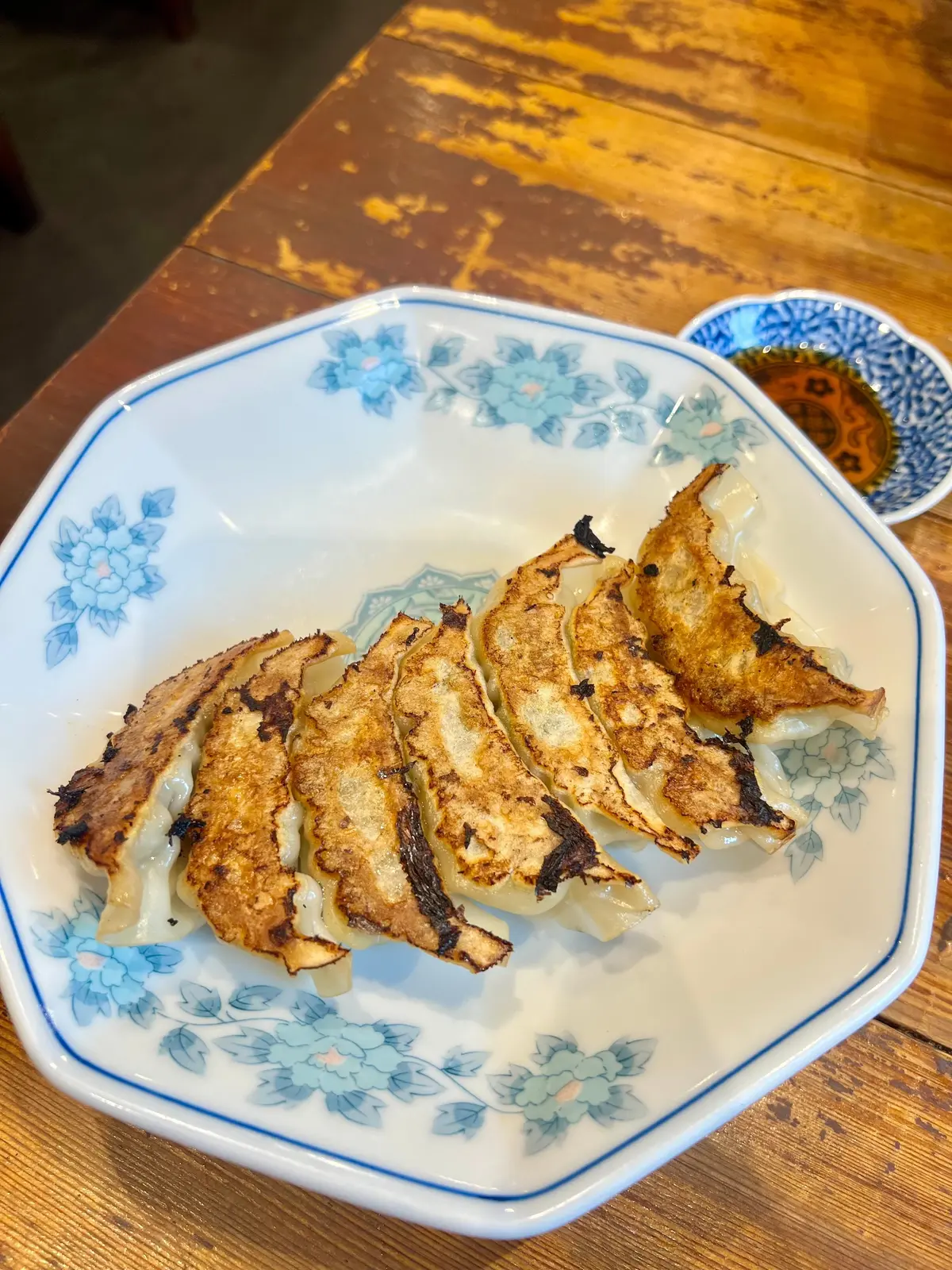 青い花模様の白い長方形の皿に焼きぎょざが並んでいる。右側に小さな青い皿にタレが入っている。