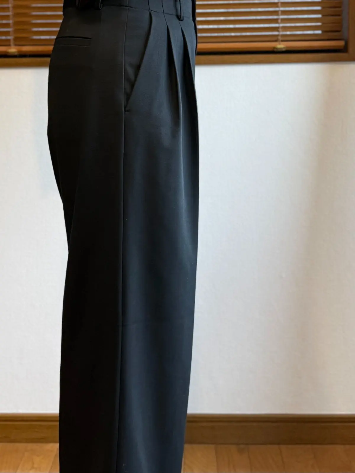 ユニクロスマートワイドストレートパンツ、黒いハイウエストのゆったりとしたパンツ。フロントにプリーツがあり、裾に向かって細くなるシルエット。木製の床と白い壁の前で撮影。