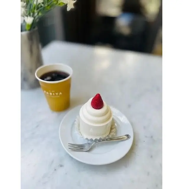 白いプレートにイチゴをトッピングした小さなケーキと、黄色いカップにコーヒーが置かれたカフェのテーブル