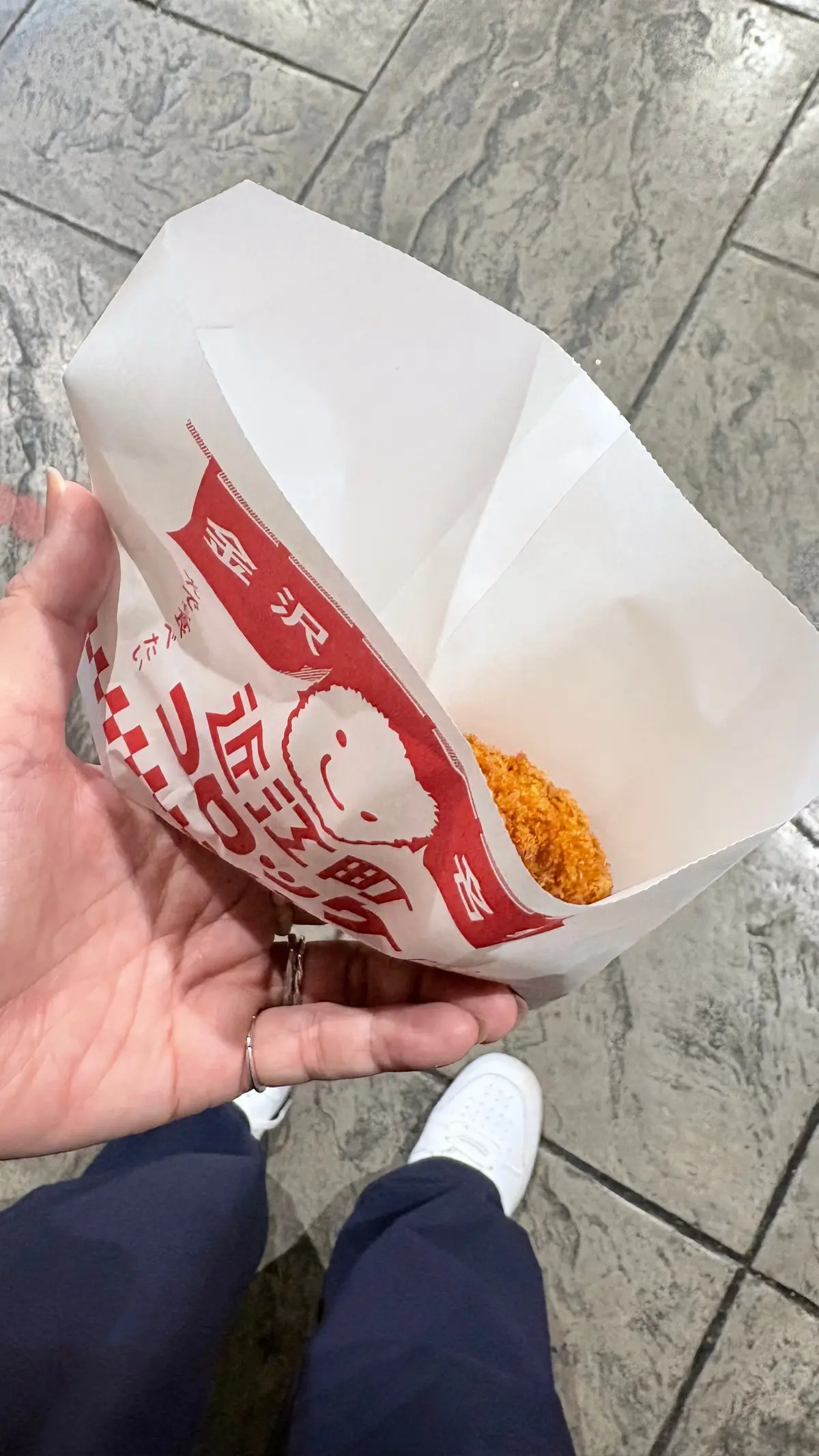 白い紙袋に入った、かしこい顔をした熊のイラストが描かれた、吉野家のお弁当。手で袋を持ち、白いスニーカーを履いた足が写っている。