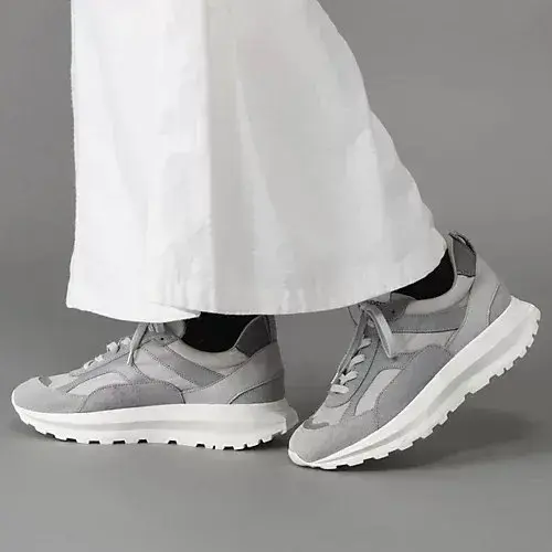 グレーのスニーカーを履いた足元。白いワイドパンツが裾から少し覗いている。靴は厚底で、左右に配置されている。