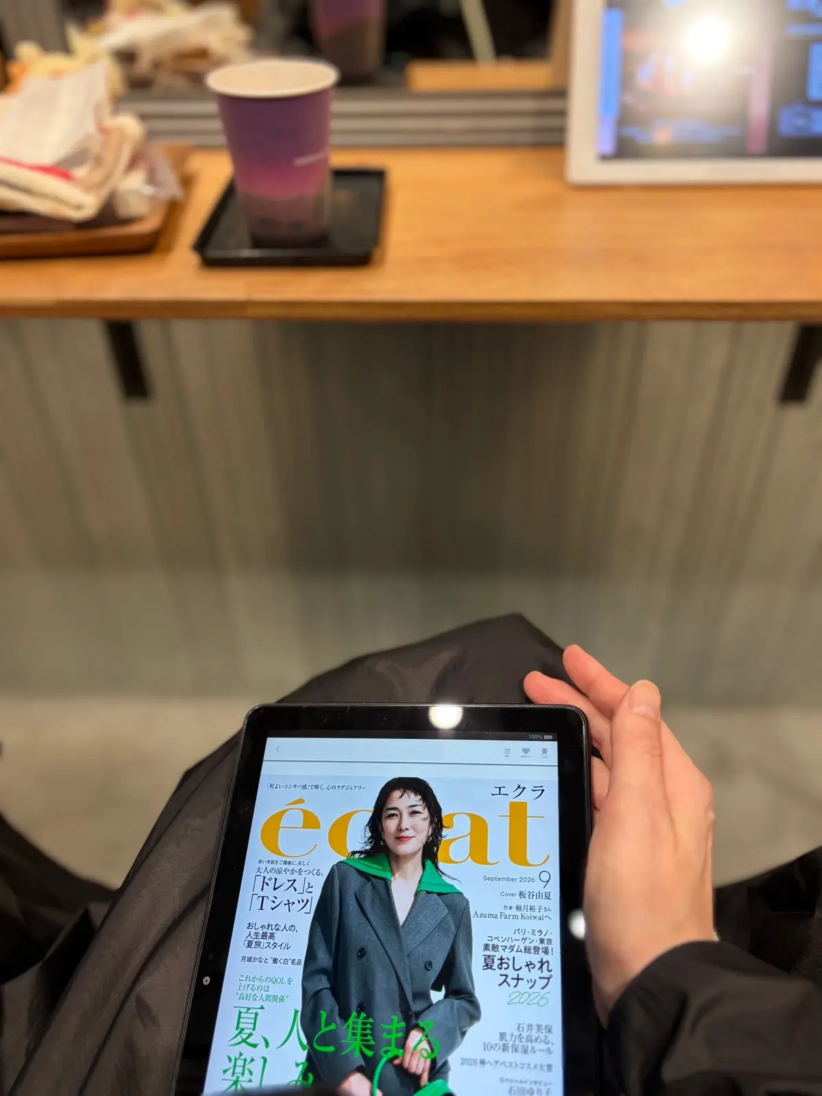 美容室でカットを受ける女性。黒いカットクロスとオレンジ色のタオルを着用し、スマートフォンで自撮りをしている。後ろには美容師がハサミを持っている。