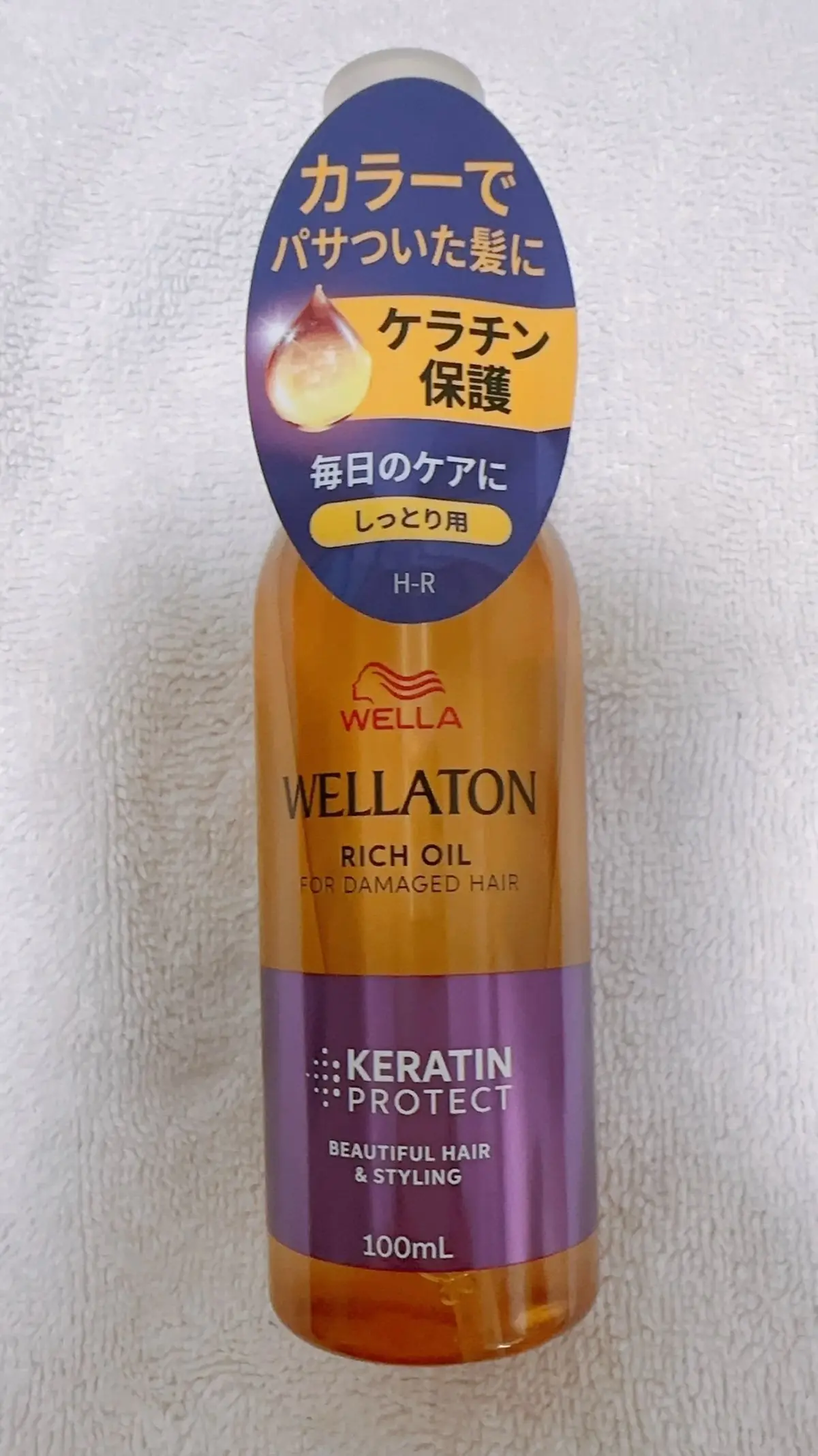 ウェラ WELLATON リッチオイル（ダメージヘア用）100ml。オレンジとゴールドのボトルで、前面にブランドロゴと「ケラチン保護」の文字。黄色の吹き出しには「カラーでパサついた髪に」などの日本語のキャッチコピー。