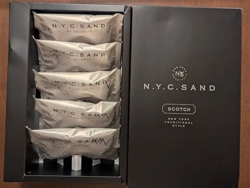 N.Y.C.SANDの黒い箱には、銀色のサンドイッチが6個入っている。箱の右側にはロゴと「SCOTCH NEW YORK TRADITIONAL STYLE」の文字が記載されている。
