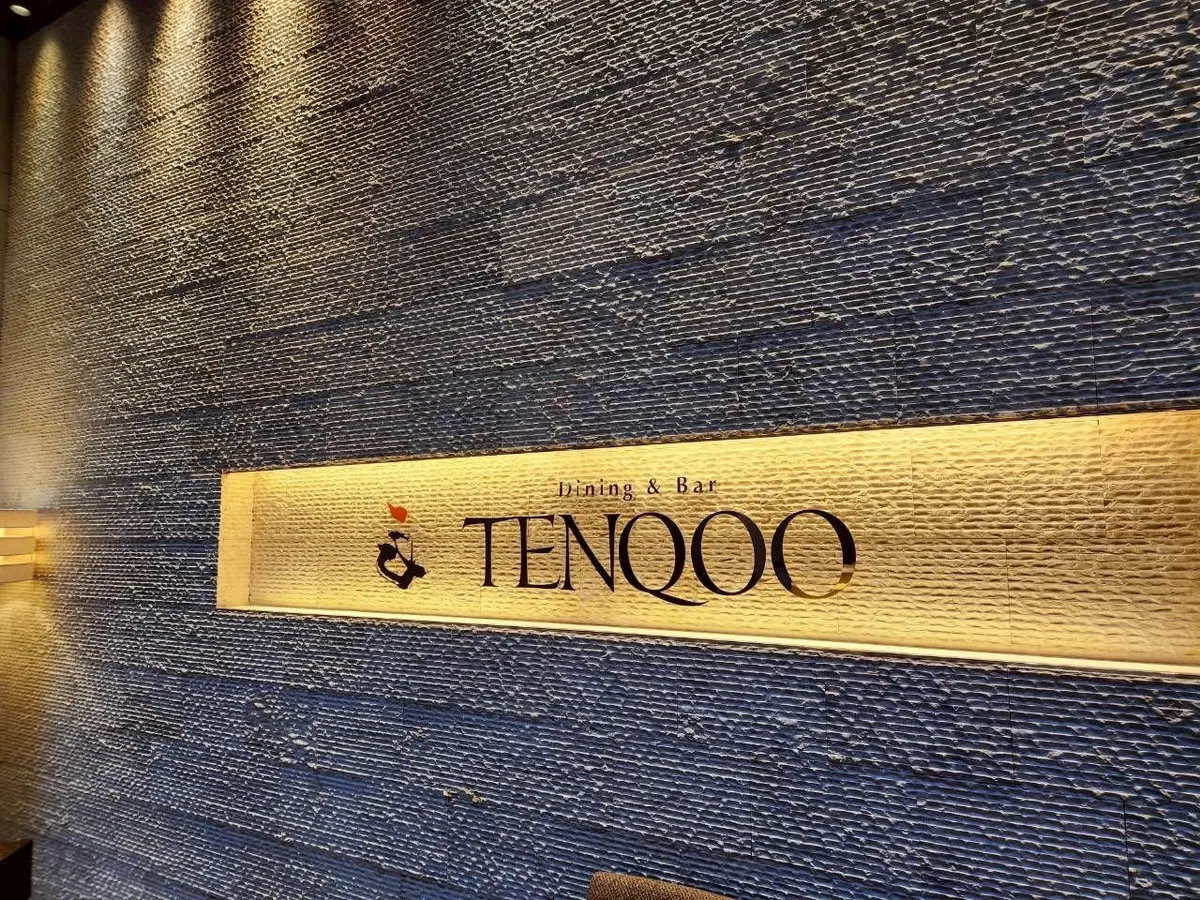 金色のプレートに「TENQOO」と書かれたレストランの看板、壁はテクスチャのある青色