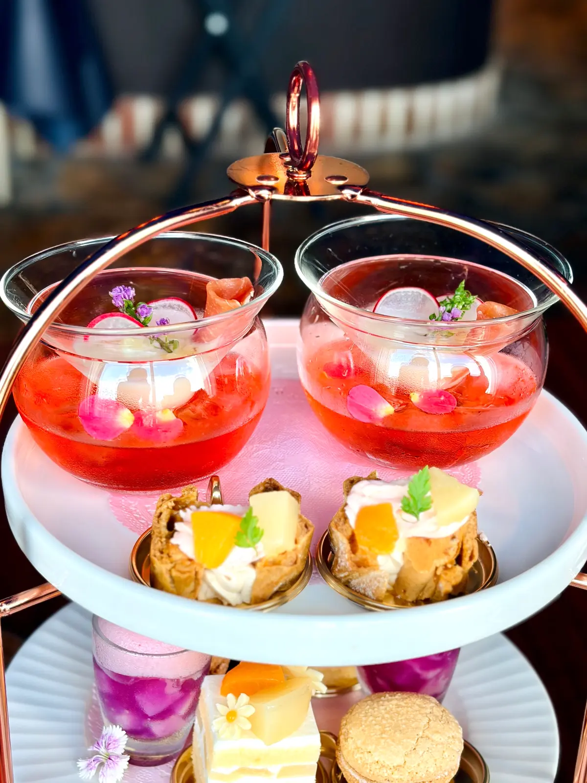 ピンク色の飲み物と、様々な焼き菓子やケーキが三段のスタンドに盛り付けられている。ロマンチックな雰囲気のティーセット。
